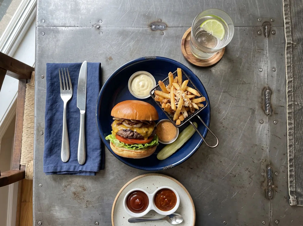 Hamburguesa con patatas y salsas en su plato azul, en la foto de partida cedida: mesa de metal junto a la ventana.